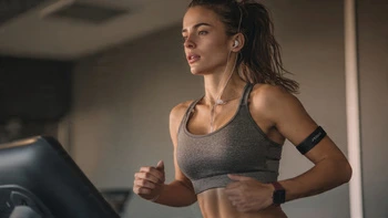 Femme sportive qui court sur un tapis de course, portant un cardiofréquencemètre en brassard et une montre connectée.